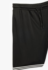 Zwarte sportshorts met een gestructureerde afwerking, elastische tailleband en koord. Voorzien van witte gestreepte accenten aan de zoom.