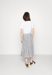 T-shirt blanc associé à une jupe midi imprimée florale noir et blanc, avec une forme évasée, portée avec des chaussures de sport noires et beiges.