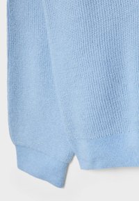 Manche de pull tricoté bleu clair avec poignet côtelé montrant une texture de point détaillée sur fond blanc.