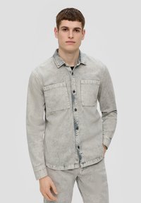 Lichtgrijze denim shirt met een vervaagde uitstraling, knoopsluiting aan de voorkant, twee borstzakken en lange mouwen. Beschikt over een standaard kraag en gestikte details.