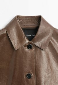 Manteau en cuir marron avec col large et pointu, boutons noirs, et étiquette Massimo Dutti à l'intérieur du col.