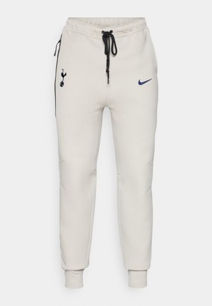 Vaaleanharmaat Nike-housut, joissa on mustat yksityiskohdat. Varustettu brodeeratulla logolla, joustovyöllä ja narulla, sekä kuminauhalla varustetuilla nilkoilla.