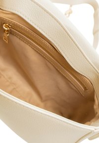 Een crèmekleurige handtas met een textuurrijk buitenoppervlak, voorzien van een beige stoffen binnenkant en een zakje met ritssluiting voor opbergruimte.