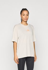 Μπεζ υπερμεγέθη μπλουζάκι με κοντά μανίκια, στρογγυλή λαιμόκοψη, με μικρό πορτοκαλί λογότυπο της μάρκας στο στήθος. Μαλακό, ελαφρύ ύφασμα.