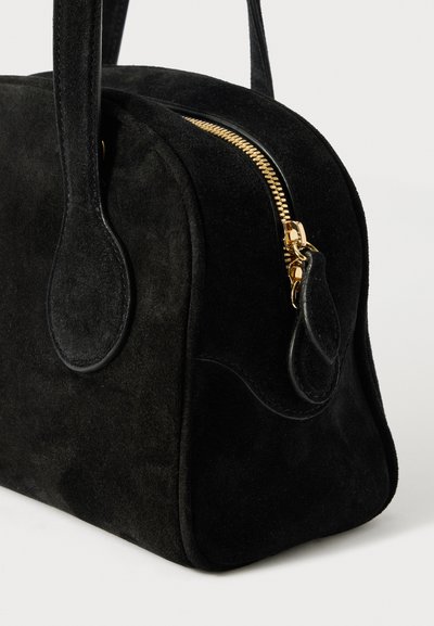 Schwarze Wildlederhandtasche mit runder Form, goldenem Reißverschluss und glatten Lederakzenten. Doppelte Tragegriffe. Minimalistisches Design.