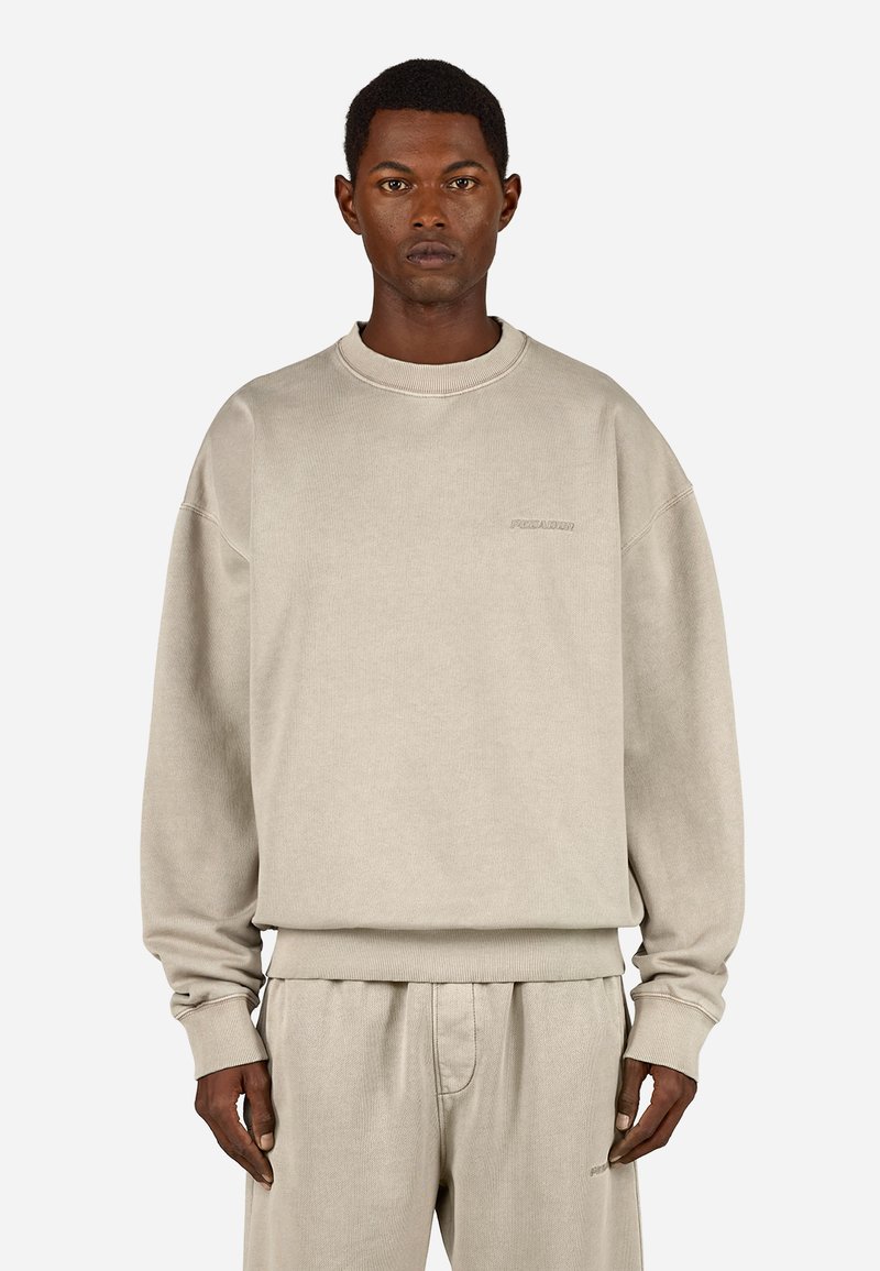 Svetlo béžová mikina s okrúhlym výstrihom, ribbovanými manžetami a vyrazeným logom na hrudi, v kombinácii so zodpovedajúcimi nohavicami.