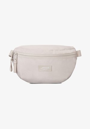 Pañuelo de tela cremosa, con cremallera y una textura suave. Presenta una pequeña etiqueta con el logo, forma redondeada y una correa lateral para facilitar el transporte.