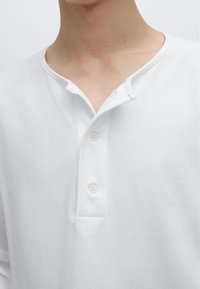 Weißes Baumwoll-Henley-Shirt mit schmalem Kragen, drei-Knopf-Leiste und glatter Textur. Genähte Kanten, keine sichtbaren Muster.