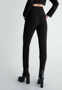 Zwarte op maat gemaakte broek met een slim fit, een hoge taille, ritssluiting en een strakke textuur, gecombineerd met glanzende zwarte platformlaarzen.