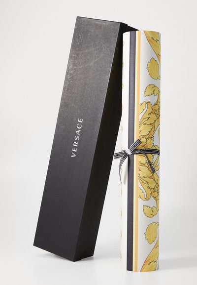 Dárková krabička Versace s cylindrickou bílou trubicí, zdobená žlutými květinovými vzory a černou stuhou. Krabička je černá.