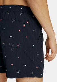 Costumi da bagno blu navy con motivi a bandiera ricamati multicolori, vita elasticizzata, tasche laterali e dettaglio della tasca posteriore.