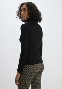 Haut à col roulé noir à côtes avec des manches longues, en forme ajustée et en tissu texturé. Associé à un pantalon taille haute à motifs.
