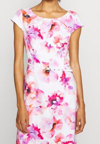 Sukienka w kwiaty z okrągłym dekoltem, krótkimi rękawami typu cap oraz białym paskiem. Posiada kolorowy, akwarelowy wzór kwiatowy w odcieniach różu i fioletu.