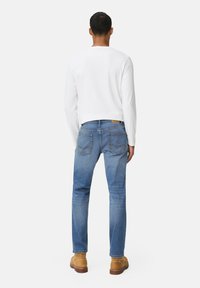 Lichtgewicht wit overhemd met lange mouwen, blauwe denimjeans met een lichte wassing, met contrasterende stiksels, en tan schoenen. Geen aanvullende details zichtbaar.