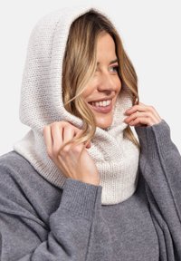 Szydełkowy kaptur w kremowym kolorze z teksturowanym wzorem, z dopasowaniem wokół szyi i głowy, zestawiony z szarym swetrem.
