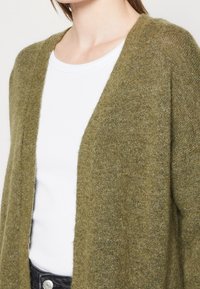 Olivgrön stickad kofta med lös passform och öppen framdesign, med en mjuk textur och minimalistisk stil.