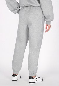 Grå sweatpants lavet af blødt stof, med elastisk linning, manchetter ved anklerne og sidelommer. Bæres med hvide sneakers.
