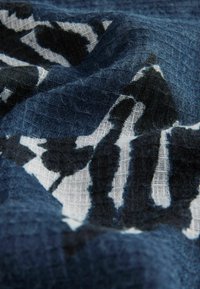 Granatowa tkanina tkana z odważnym czarno-białym abstrakcyjnym wzorem, z teksturowanym wykończeniem i miękkimi fałdami odsłaniającymi głębię.