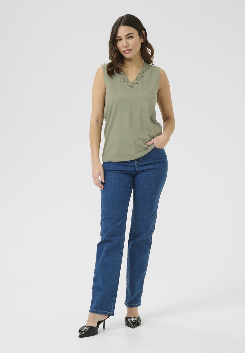 Haut sans manches vert olive avec décolleté en V et détails en dentelle, associé à un jean droit bleu et des chaussures à talons noires. Design simple.