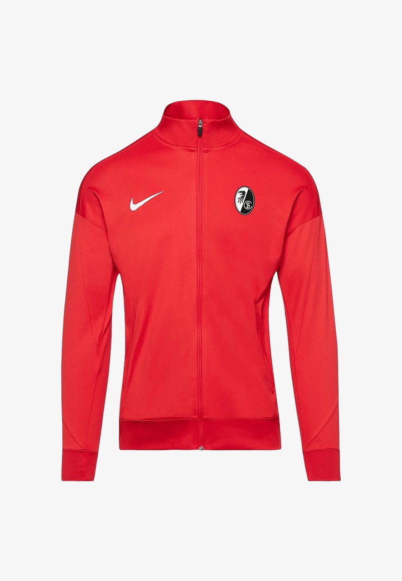 Rote Sportjacke mit vollem Reißverschluss, aus glattem Stoff, mit einem weißen Nike-Logo und einem schwarz-weißen Teamwappen auf der Brust.