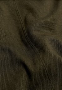 Dunkelgrüner Stoff mit feiner Waffelstruktur und einer sichtbaren, vertikal verlaufenden Naht, die leichte Falten und Schatten zeigt.