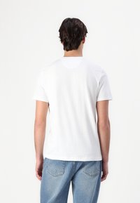 White cotton t-shirt with short sleeves, round neckline, and a relaxed fit. Back view shows plain design and smooth texture.