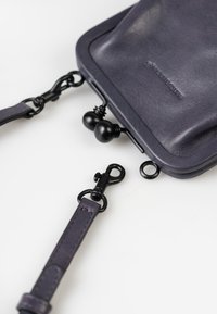 Borsa in pelle viola con una texture liscia, dotata di chiusura a fibbia, tracolla removibile e dettagli in metallo nero.