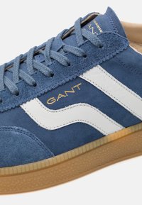 Blaue Wildleder-Sneaker mit weißen Lederakzenten, strukturiertem Gummi-Sohle und blauen Schnürsenkeln. Mit goldfarbenem "GANT"-Logo an der Seite.