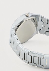 Ασημένιο ρολόι από ανοξείδωτο ατσάλι με οκταγωνική κάσα, γυαλιστερή επιφάνεια και μπρασελέ με κρίκους που φέρουν ορθογώνιες λεπτομέρειες και κορώνα.