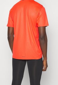 Camiseta deportiva de manga corta en naranja brillante, hecha de un tejido de malla transpirable con un acabado texturizado. Presenta la marca "AEROREADY" en la parte inferior.