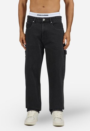 Pantalones cargo de mezclilla negra con un ajuste holgado, que cuentan con bolsillos laterales, trabillas para cinturón y un cierre de botón. Cintura con marca en blanco visible.