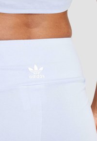 Svetlomodré priliehavé legíny zo soft materiálu s vysokým pásom, na prednej strane s bielym logom Adidas. Hladká textura.