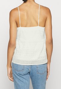 Haut en textile clair avec des détails en dentelle et des bretelles fines. Présente un design superposé et un ourlet légèrement évasé. Associé à un jean en denim.