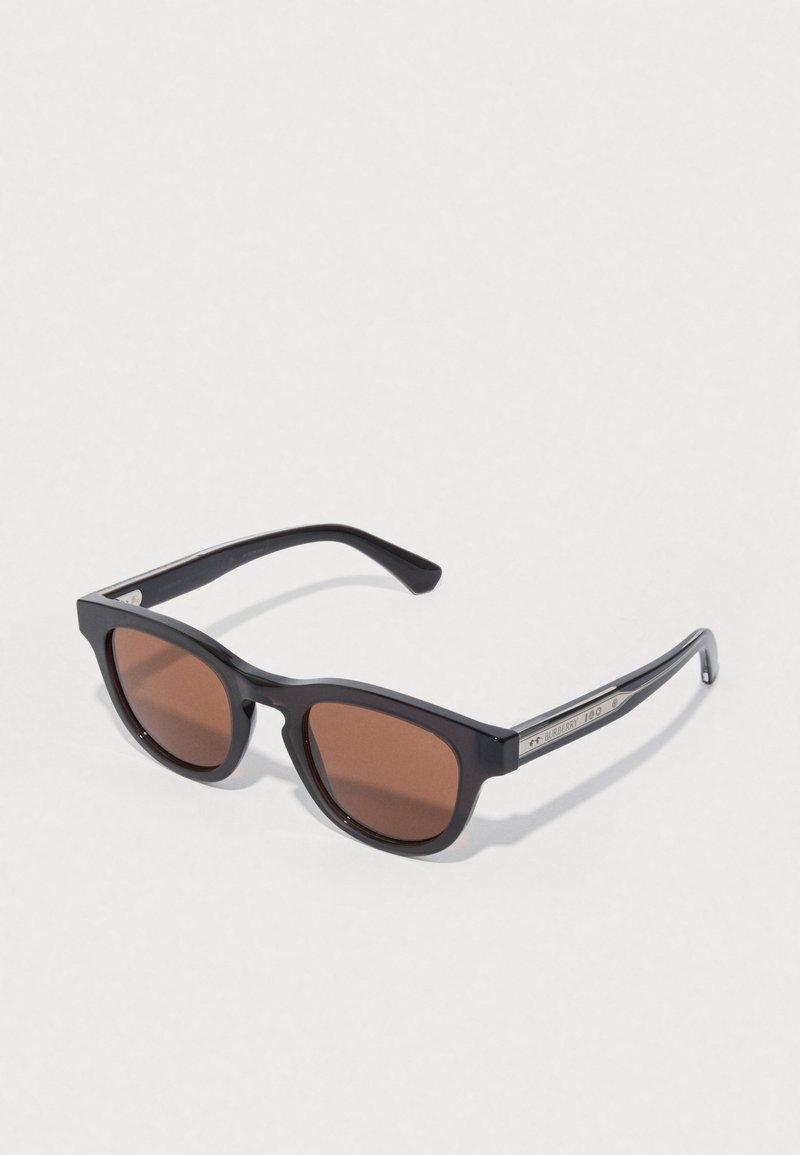 Black plastic sunglasses with brown lenses. Square frame shape with a glossy finish. Metal accents on the temples with branding details.