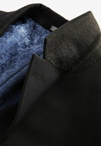 Schwarze Jacke aus strukturiertem Stoff, mit einem grauen Wollkragen und einem blauen gemusterten Futter. Innendetails umfassen Nähte.