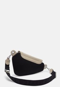 Czarna torba na ramię z siateczki i beżowej skóry o unikalnym kształcie, z teksturowanym boku i regulowanym paskiem z wytłoczonym logo.