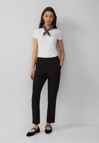 Top blanc à manches courtes côtelé avec des bords scallopés, associé à un pantalon noir ajusté et des ballerines noires, rehaussé d'un foulard noir.