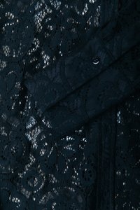 Tessuto in pizzo nero con motivi floreali e intagli intricati, con un dettaglio di manica nera solida, che mette in risalto la texture e i dettagli.