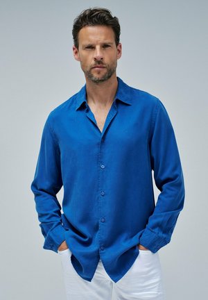 Blauwe overhemdd met een kraag, lange mouwen en een losse pasvorm. Gemaakt van gladde stof, met subtiele knopen aan de voorkant en manchetten.