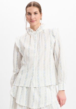 Weiße Bluse mit floralem Muster in Blau- und Gelbtönen, Rüschensaum, und langen Ärmeln mit schichtartigen Saumdetails.