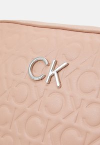Borsa a tracolla rosa con texture, caratterizzata da un motivo in rilievo e un accento in metallo argentato con logo CK sulla parte anteriore. Finitura in pelle liscia.