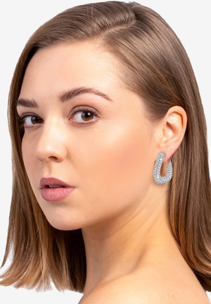 Silberne Creolen mit einer strukturierten Oberfläche, im U-förmigen Design, großer Größe und sicherem Verschluss, getragen von einem Modell mit glattem Haar.