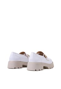 Scarpe in pelle bianca con una suola beige spessa, dotate di una fibbia d'accento dorata e una punta arrotondata. Texture liscia con dettagli cuciti.