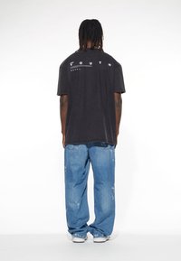 Schwarzes übergroßes T-Shirt mit weißem "YOUTH"-Grafik auf dem Rücken, kombiniert mit locker sitzenden, ausgebeulten blauen Jeans und weißen Sneakern.