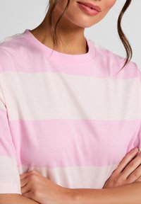 Ροζ ανοιχτό και εκρού ριγέ μπλουζάκι με κοντά μανίκια, στρογγυλή λαιμόκοψη, μαλακό βαμβακερό υλικό, διαθέτει οριζόντιες ρίγες διαφορετικού πλάτους.