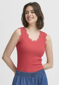 Punane sooniline tank top, millel on laineline pitsääris õlgadel ja kaelusel, kombineeritud siniste paelaga pükste kanssa.