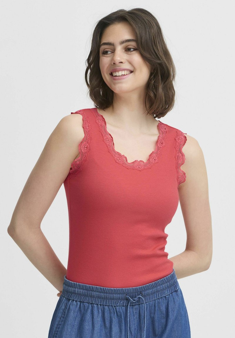 Punane sooniline tank top, millel on laineline pitsääris õlgadel ja kaelusel, kombineeritud siniste paelaga pükste kanssa.