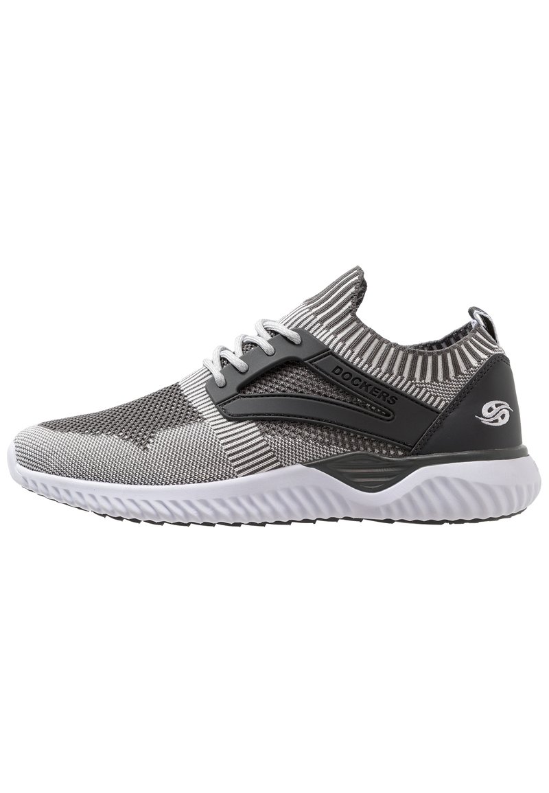 Zapatilla deportiva de punto gris con un cuello acanalado, acentos negros y una suela blanca texturizada. Presenta cordones y un detalle de logo en el talón.