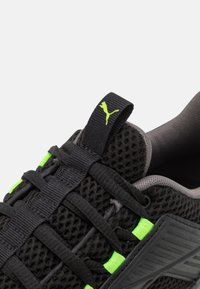 Black athletic shoe with mesh upper, features neon green accents and laces, textured overlay, and a rubber sole. Small logo on heel tab.