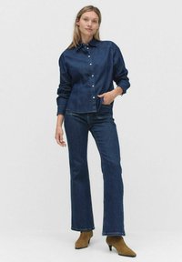 Mörk denimskjorta med knappar och långa ärmar, kombinerad med matchande utsvängda jeans. Bruna ankelboots fulländar outfiten.